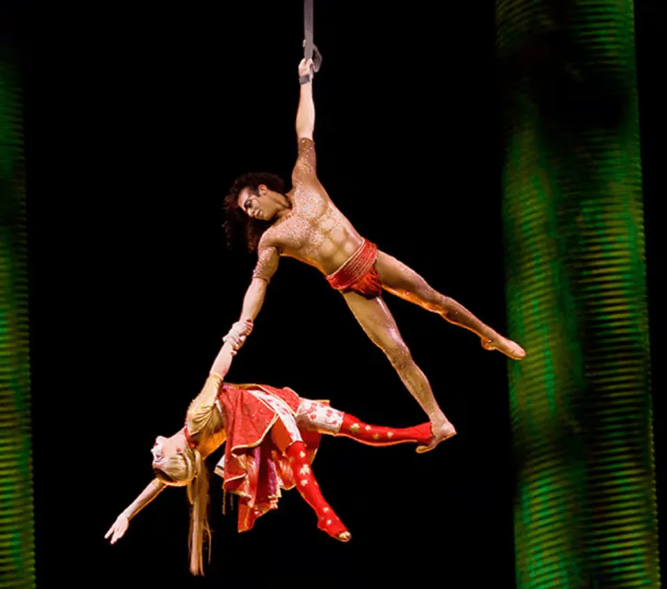 Two KÀ aerial performers suspended against a dark background