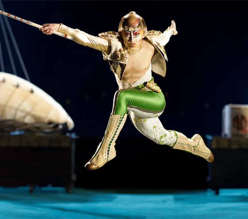 KÀ performer in green trousers leaping across the stage