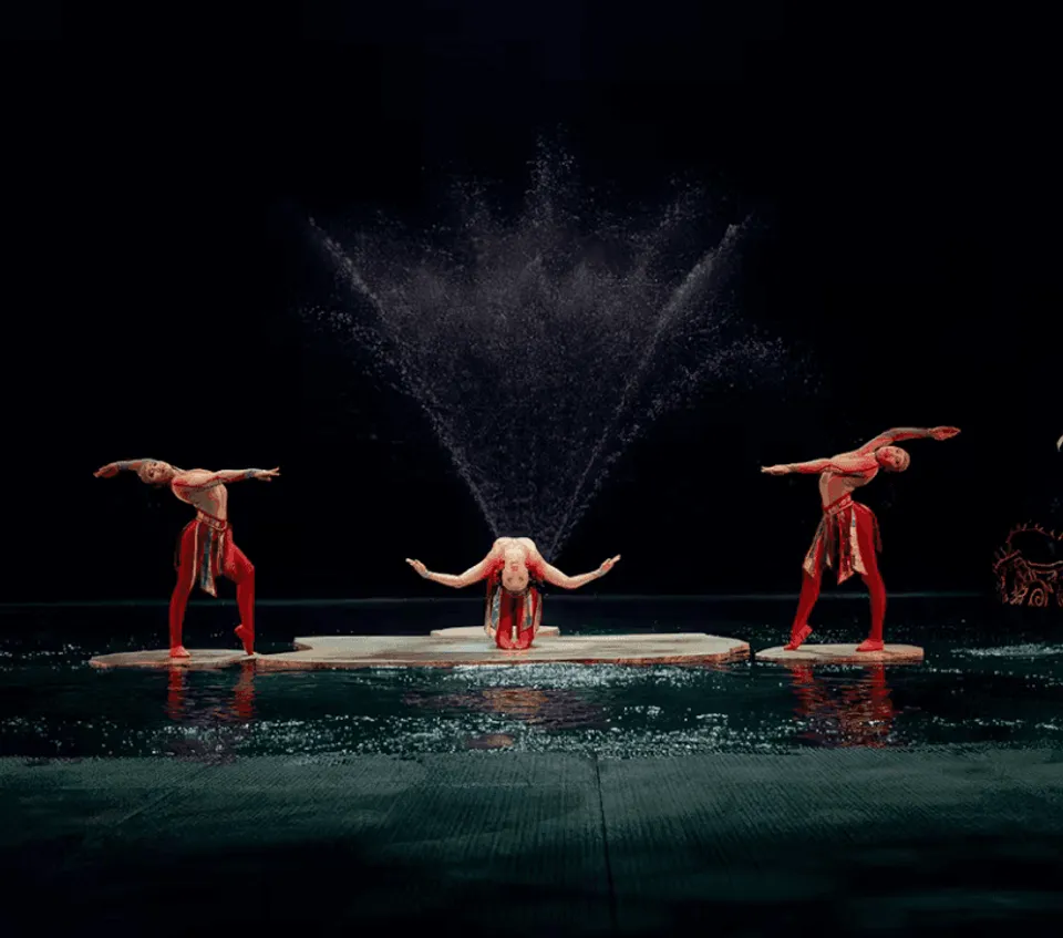 Three O performers with splashing water across the dark aquatic stage