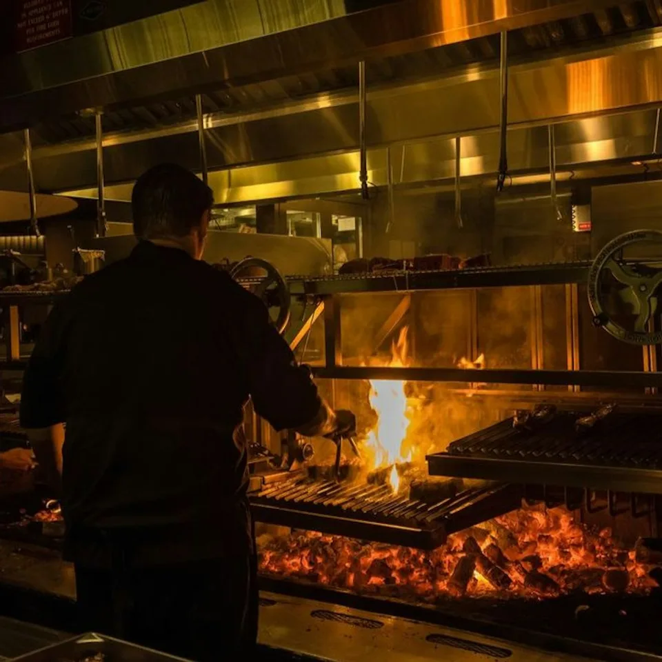 A chef cooking over flames in a steakhouse kitchen