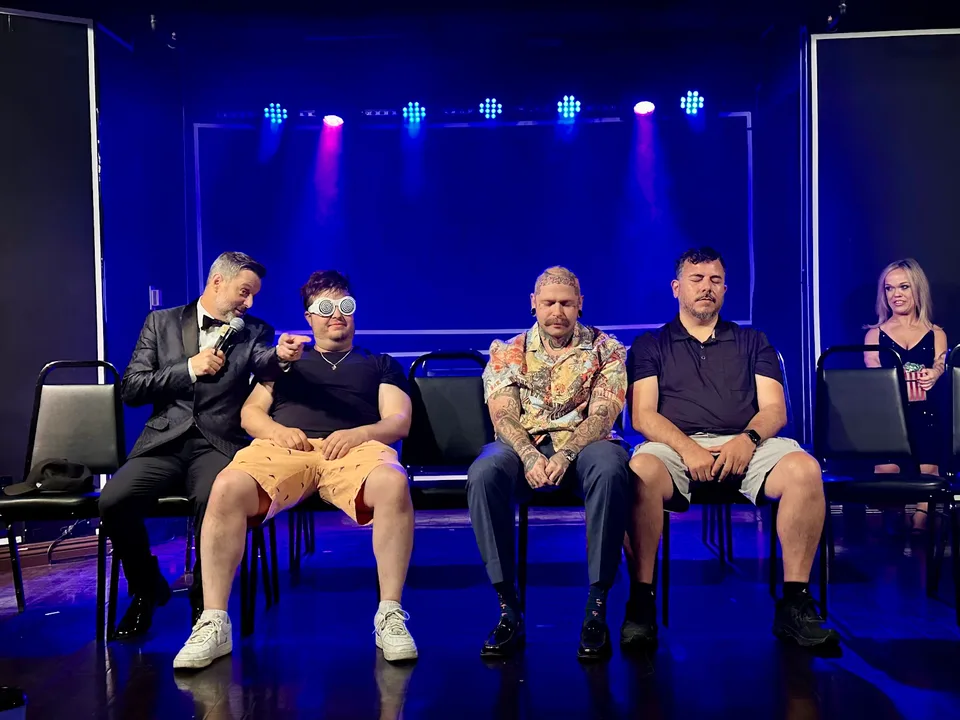 Steve Falcon with seated volunteers on a blue-lit stage