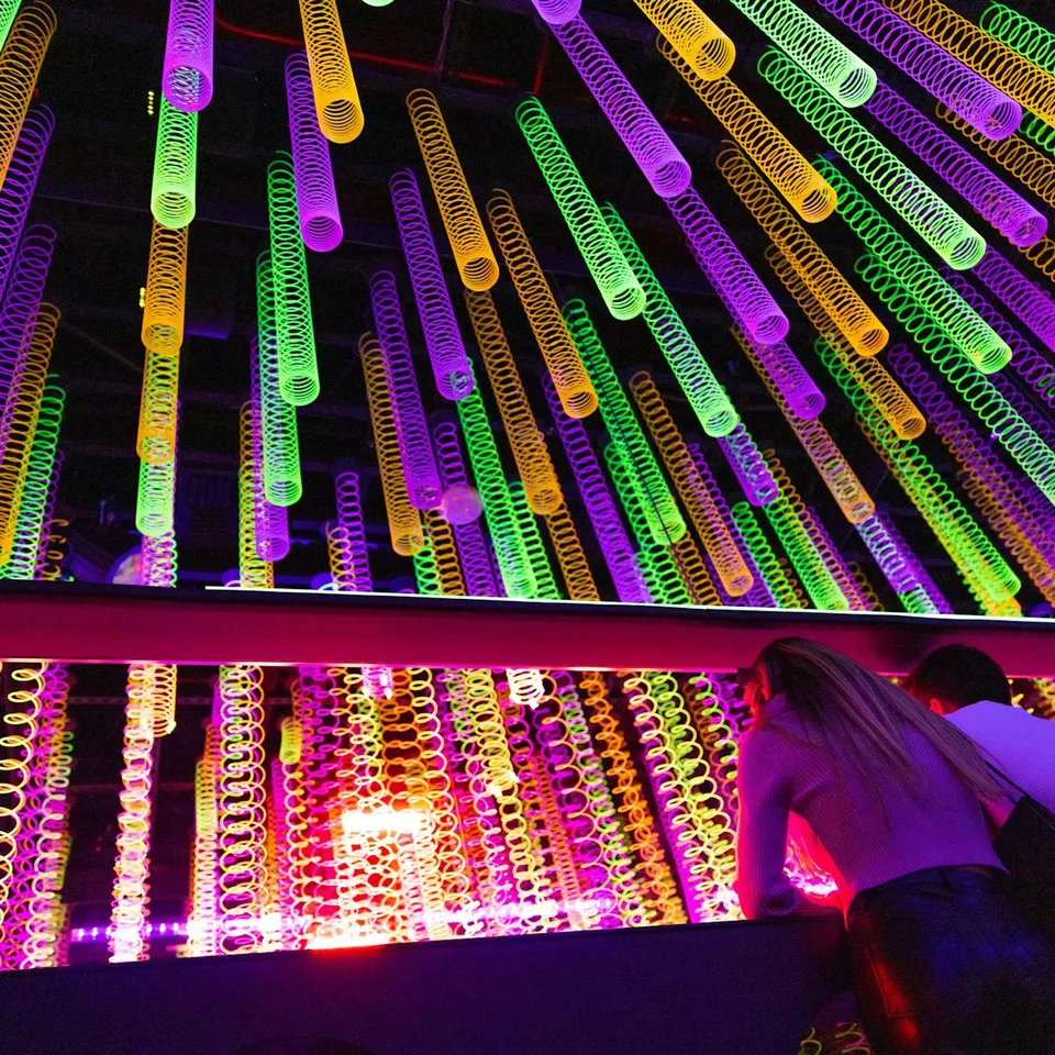 Suspended coloured light tubes in a Wink World mirror room